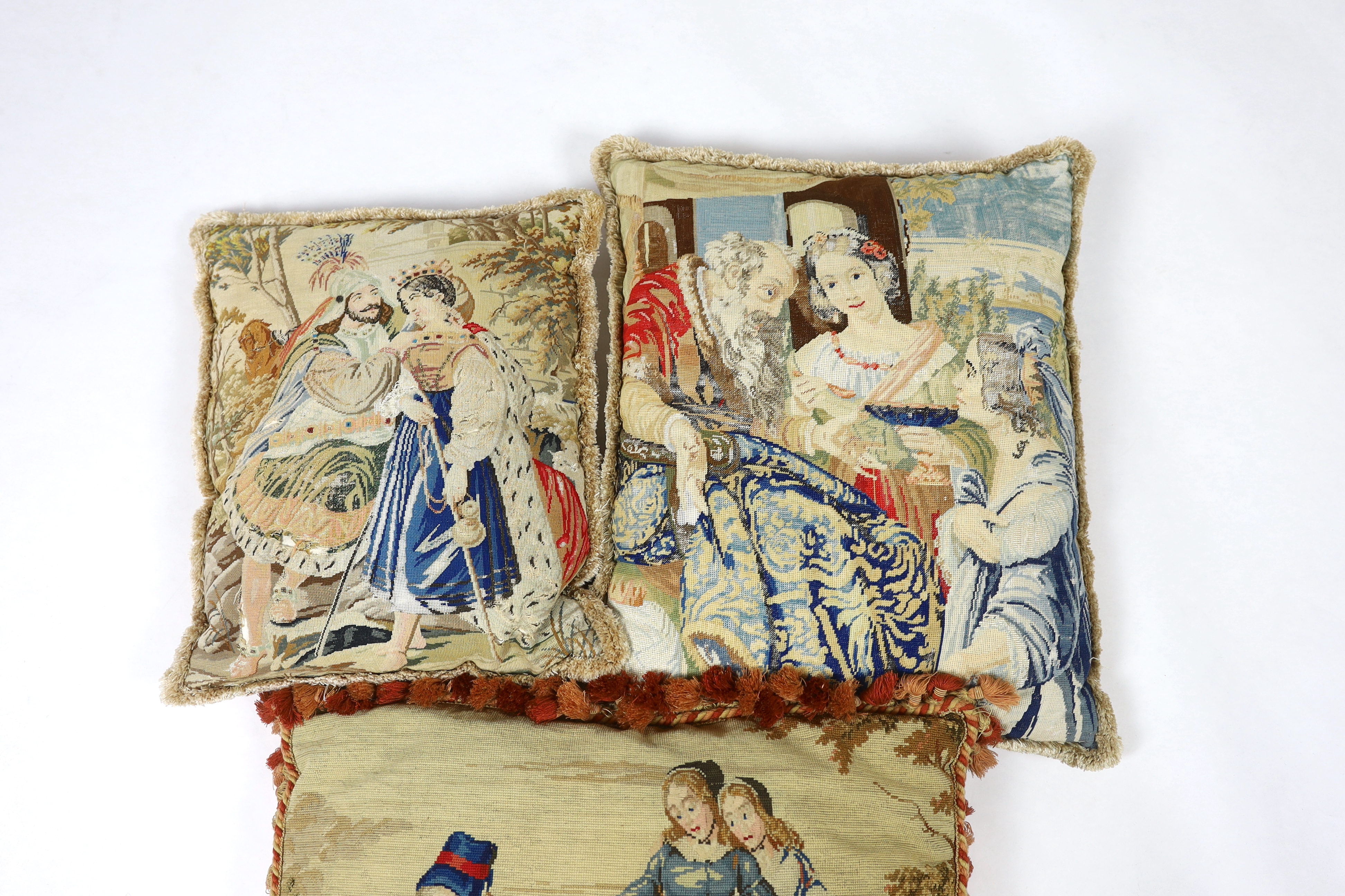 A very large Victorian Berlin wool worked cushion of possibly Queen Victoria's daughters on horseback being led by a gentleman in uniform, the cushion is edged with red tasselling, together with two similar Victorian Ber